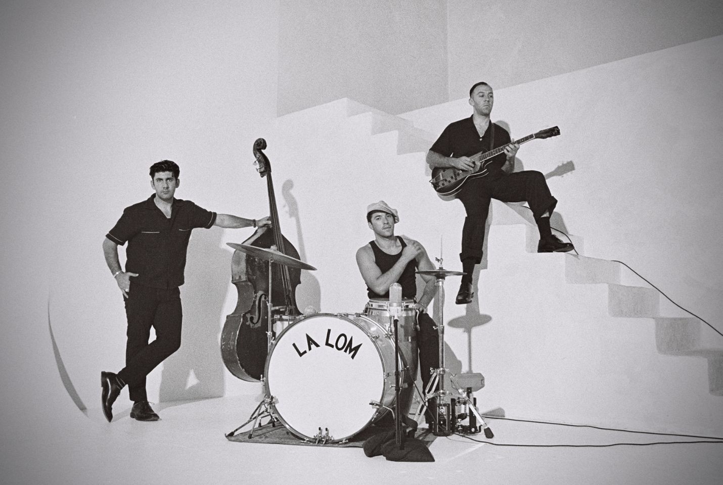 A black and white image of three men dressed in black by a staircase with instruments